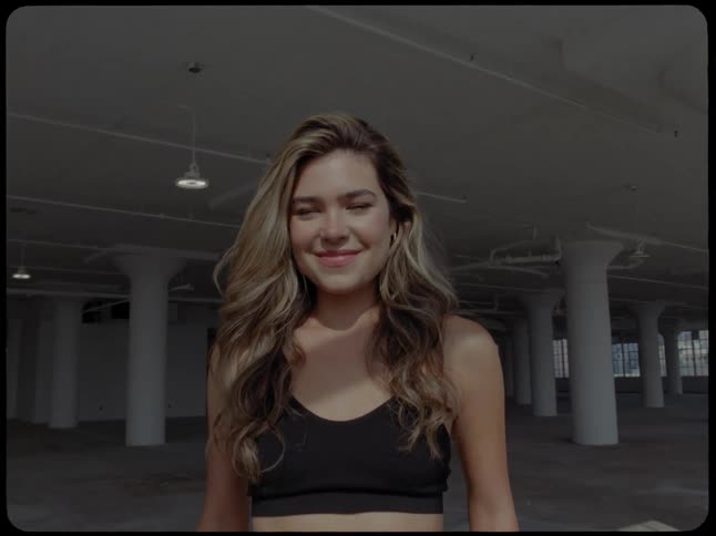 A beautiful young woman with blonde hair smiles warmly while standing in a large, empty industrial loft