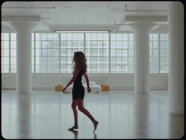 A woman walks and dances thoughtfully through an empty, sunlit industrial loft apartment