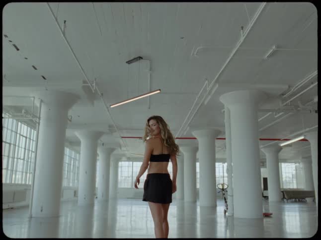 Slow motion shot of a stylish woman walking through a large, empty industrial loft and turning to face the camera