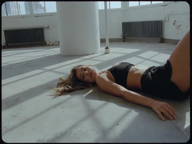 A tired young woman in athletic wear rests on the floor of a sunlit industrial loft after a workout