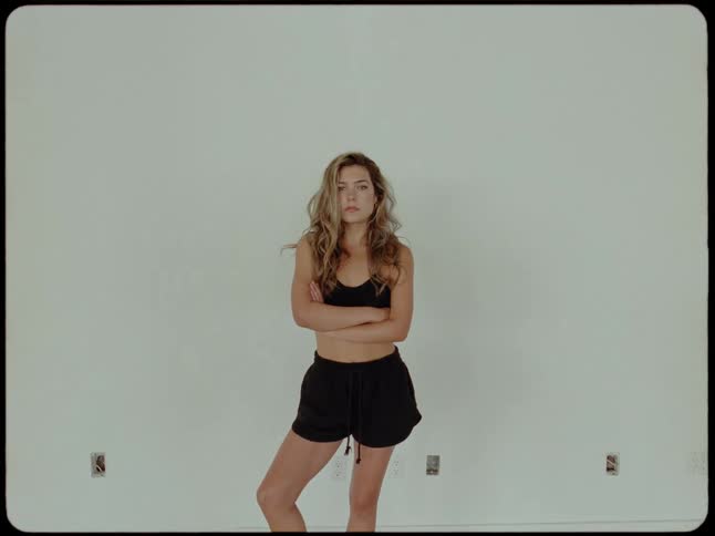 A confident woman in athletic wear crosses her arms and poses against a plain white wall in a vintage film style shot
