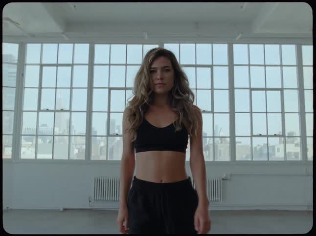 Slow motion shot of a determined woman in athletic wear walking towards the camera in a spacious city loft