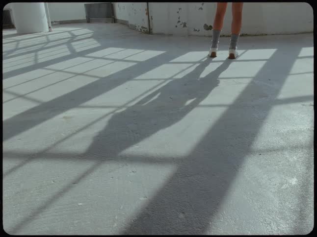 The shadow of a woman standing in a sunlit industrial loft is cast across the concrete floor
