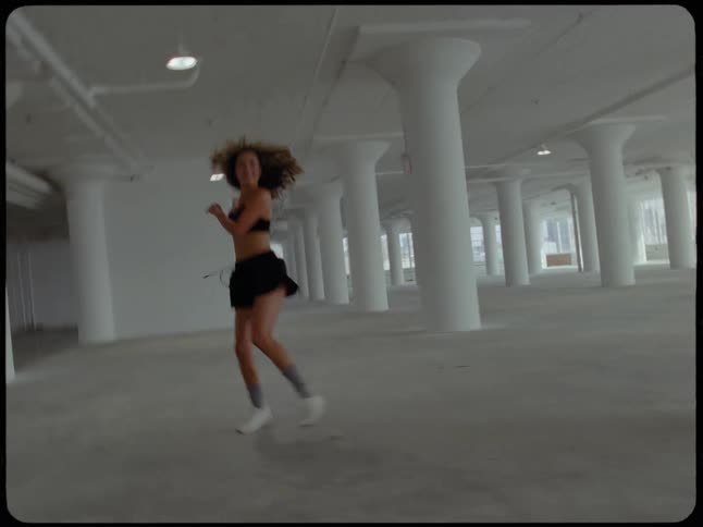 Slow motion retro footage of a joyful young woman running and skipping through a spacious industrial loft