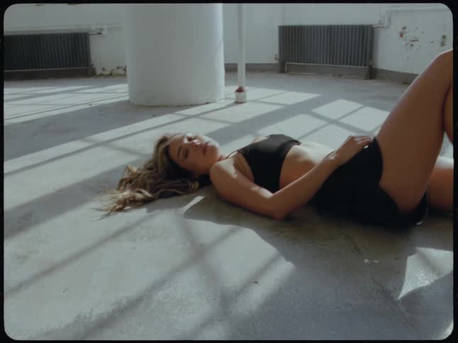 A young woman in sportswear rests on the floor of a sun-drenched, empty loft space