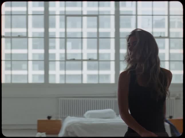 A pensive woman in a black top walks in slow motion through her minimalist city loft apartment