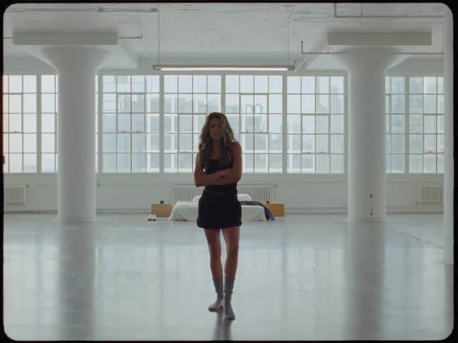 A serious woman stands with arms crossed in an empty city loft as the scene is overexposed by a bright white light