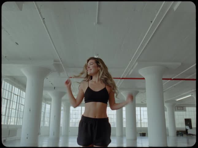 A confident woman in athletic wear poses and walks through a bright, spacious industrial loft in slow motion