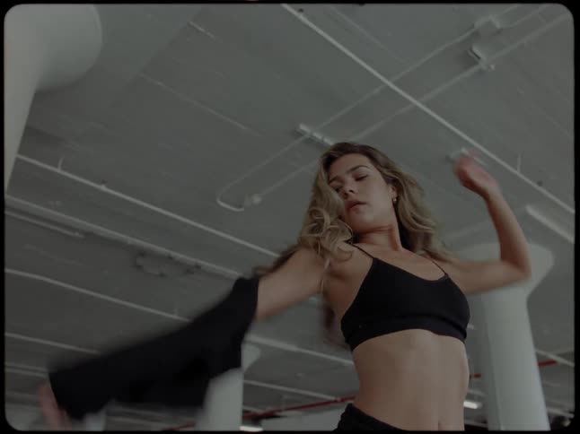 A female dancer in an industrial loft slowly removes her shirt before beginning an expressive dance routine