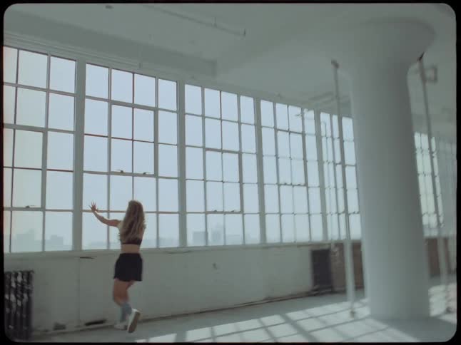 A young woman joyfully runs and dances with freedom through a large, empty, sunlit industrial loft with large windows