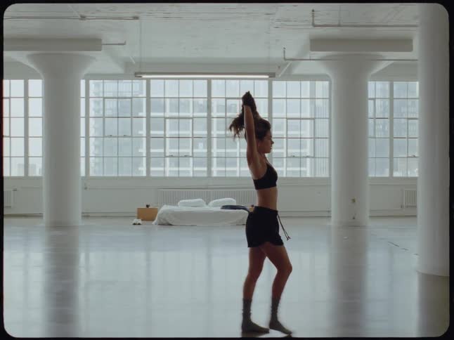 Slow-motion shot of a woman walking through a large, empty city loft apartment as she takes off her shirt