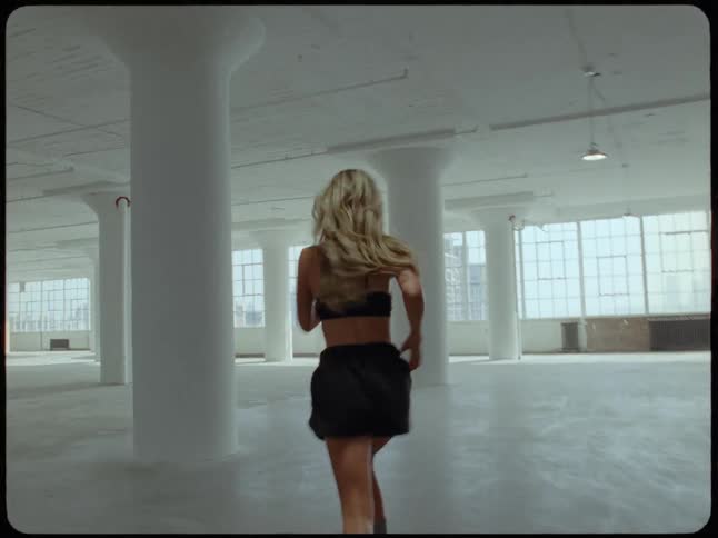 Vintage style footage shows a woman running joyfully through a large, empty industrial loft space