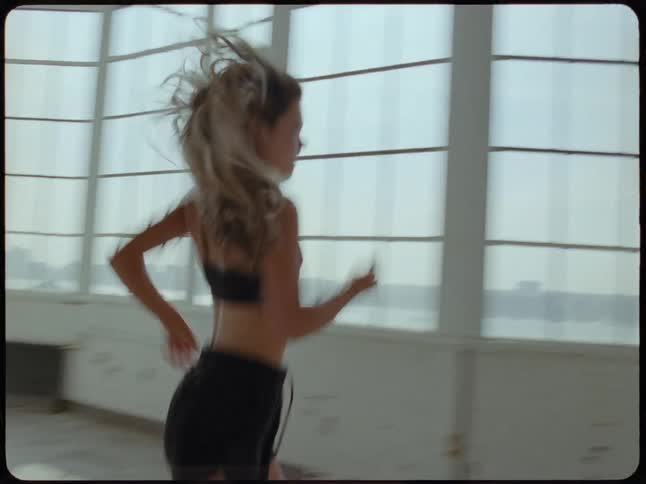 Slow motion footage of a fit woman in athletic wear running with determination through a sunlit industrial loft