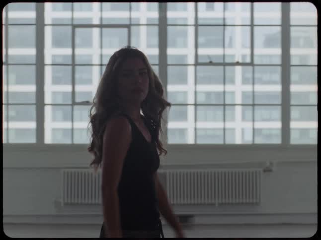 A pensive woman in silhouette walks slowly through a spacious urban loft apartment with large windows