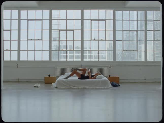 A person relaxes while reading a book in bed in a spacious minimalist loft with large windows