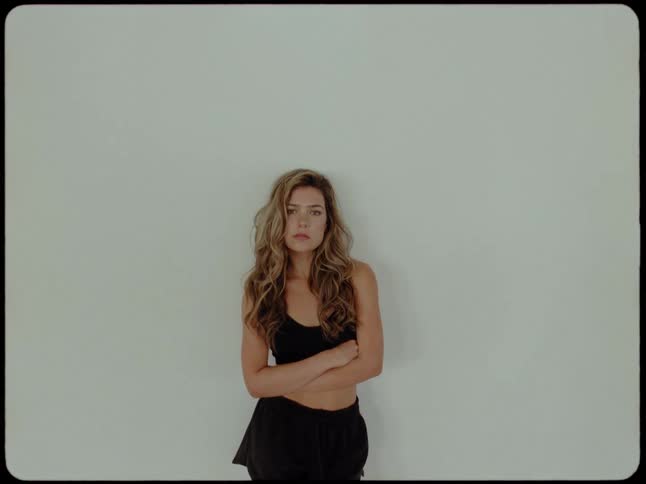 A serious young woman in athletic clothes stands with her arms crossed against a plain wall in this vintage-style footage