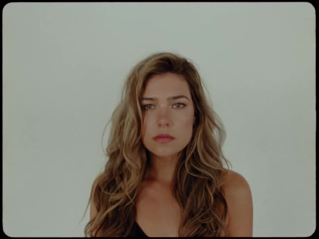 A close-up portrait of a pensive woman with long wavy hair slowly opening her eyes and looking at the camera