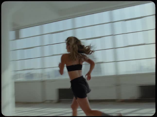 A woman runs in slow motion through a sunlit, empty industrial loft space with large windows