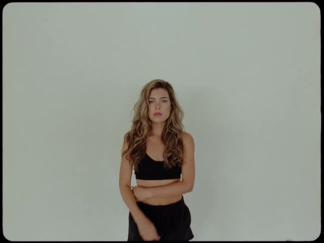 A pensive young woman in athletic wear looks directly into the camera as it slowly zooms in for a close-up against a plain background