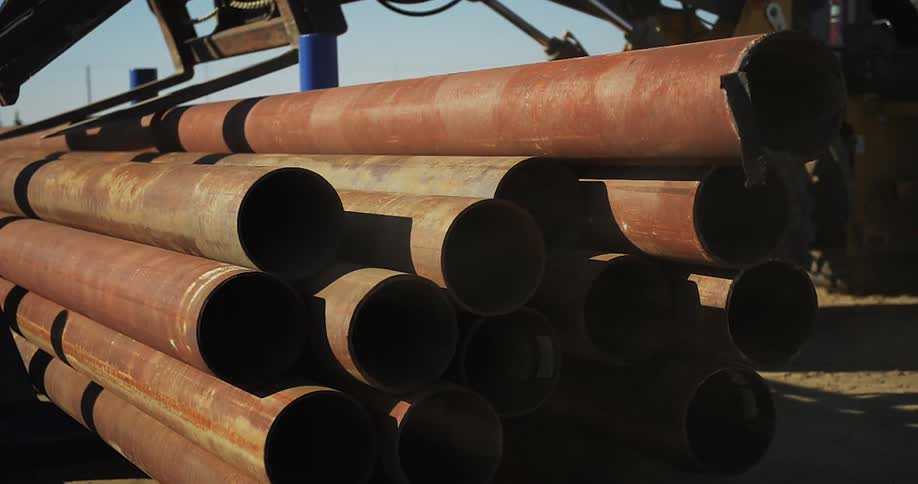 A forklift stacks large metal pipes