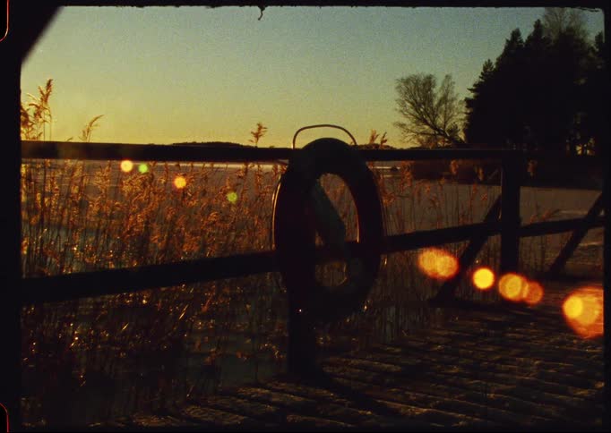 A lifebuoy hangs on a wooden pier overlooking a frozen, snow-covered lake during a golden sunset, shot on vintage film