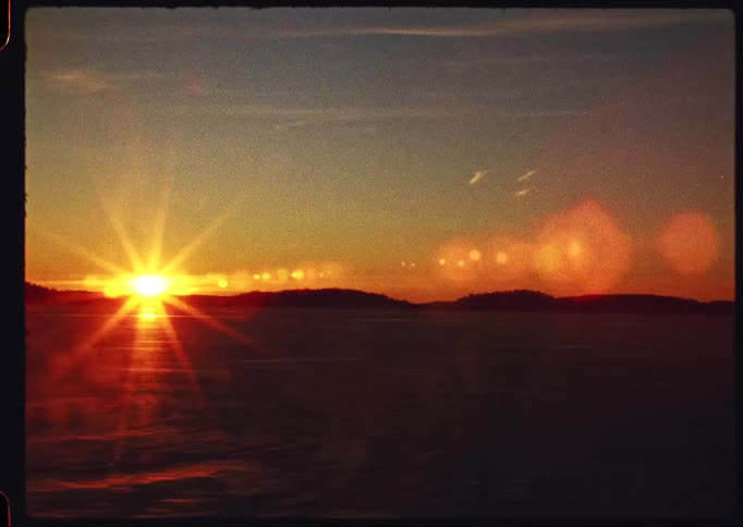 A nostalgic home movie style shot captures the sun setting over a frozen landscape with a large, beautiful lens flare