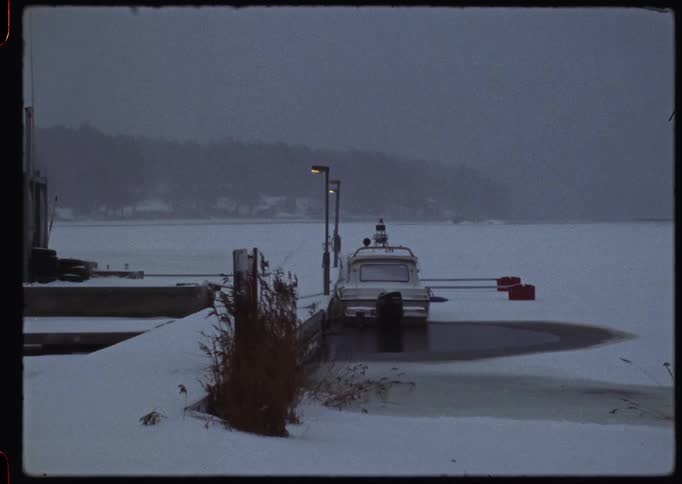 A still, vintage shot of a lone boat frozen in at a snow-covered dock on a bleak winter's day