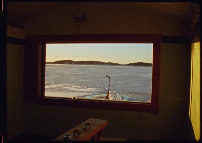 A peaceful view from an ice fishing hut window overlooking a vast, frozen lake during a winter sunset