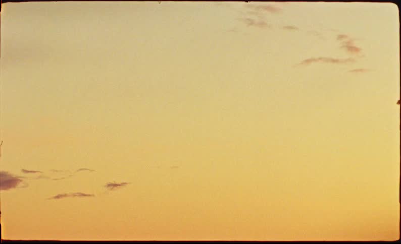 Vintage 8mm film captures a static shot of a warm, golden sky at dusk or dawn