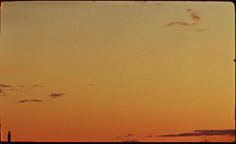 A vintage film capture of a warm orange sunset sky with a silhouetted cityscape along the horizon