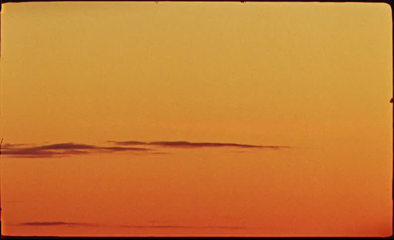 A minimalist vintage film shot captures the warm orange glow of a serene sky at sunset with thin clouds