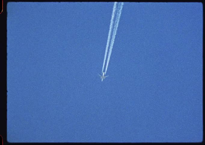 A vintage film-style shot captures an airplane flying high in a clear blue sky, leaving a white contrail behind it