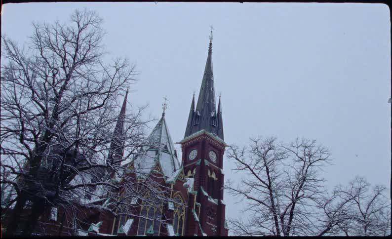 An old film captures a majestic, snow-covered church with a prominent clock tower against a grey winter sky