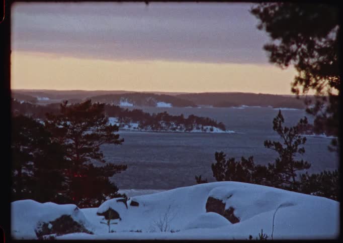 A vintage timelapse captures a winter sunset fading over a snowy landscape overlooking a vast sea with scattered islands