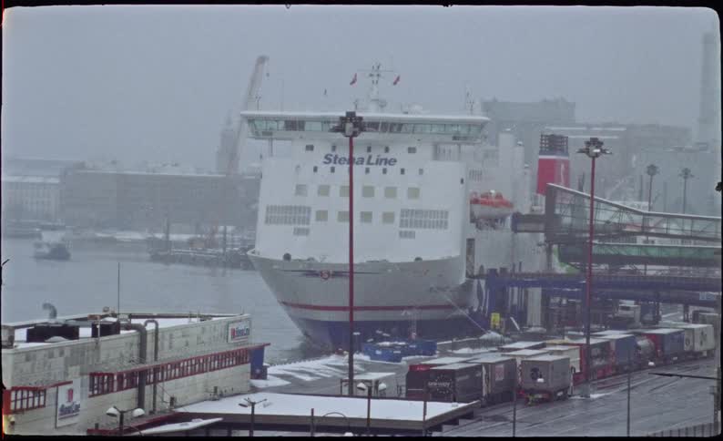 A Stena Line ferry is docked at an industrial port as snow falls during a winter day