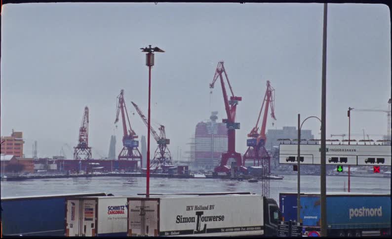 Vintage film footage shows a snowy, industrial harbor with large red cranes and semi-trucks in the foreground