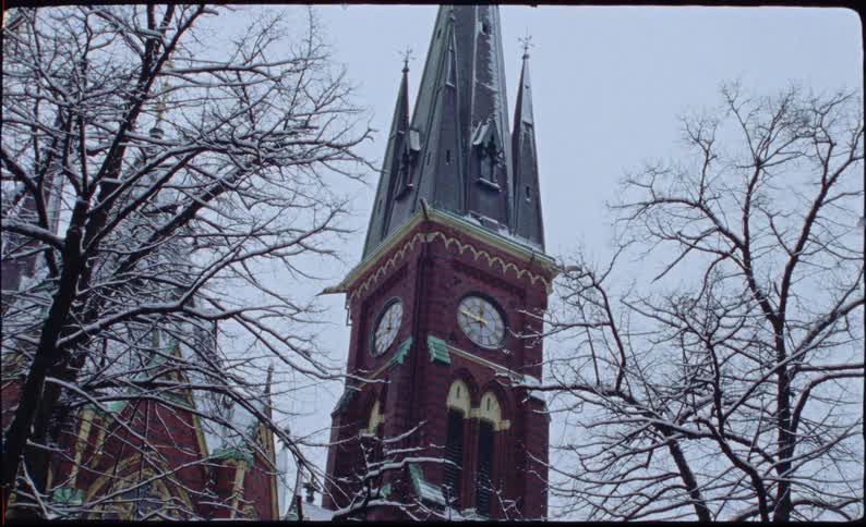 Vintage film captures a static view of a historic red brick church clock tower on a snowy winter day
