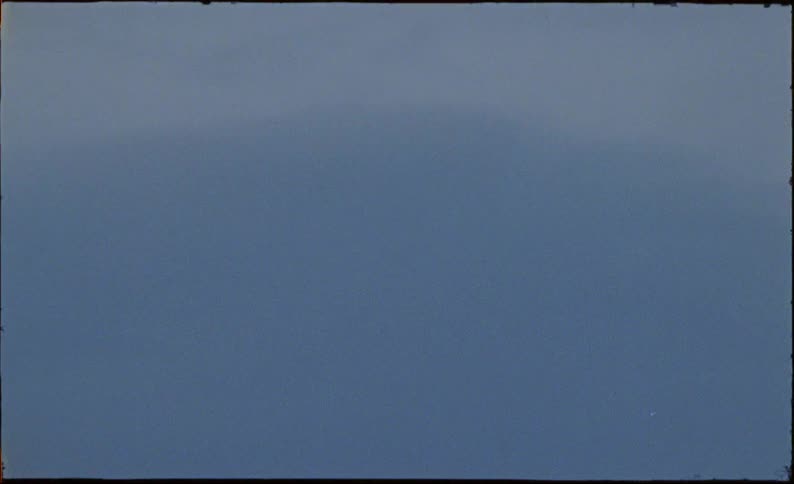A slow-motion vintage shot follows a flock of black crows as they fly across the cloudy, grey sky