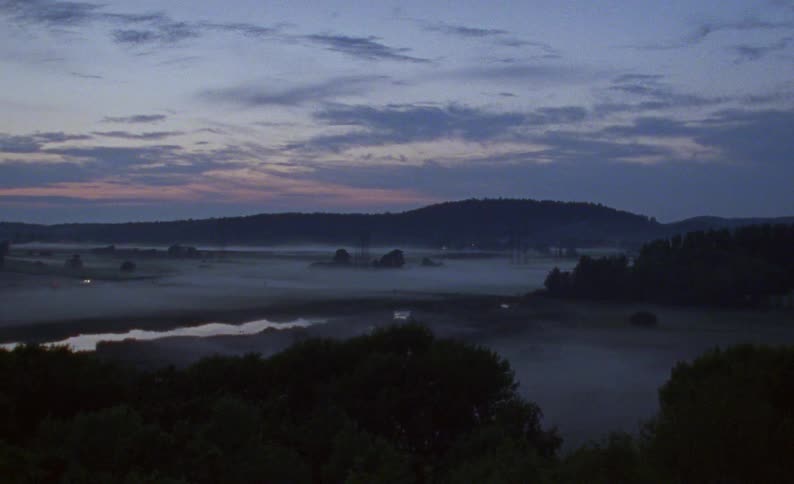 A serene, wide shot of a river valley blanketed in thick fog during the quiet moments of twilight