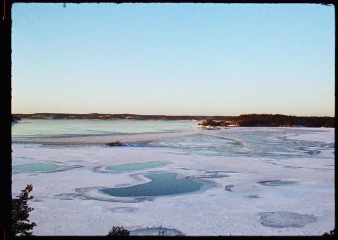 A vintage Super 8 film captures a slow pan across a serene, frozen archipelago in winter, with snow-covered ice and silhouetted trees against the dawn sky