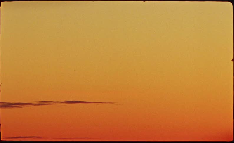 A distant airplane soars across a vast, warm orange sky during a minimalist sunset, captured on vintage film