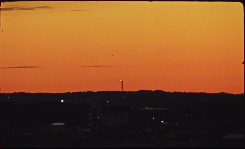 16mm film captures the silhouette of a city with a gas burning tower a vibrant orange sunset sky