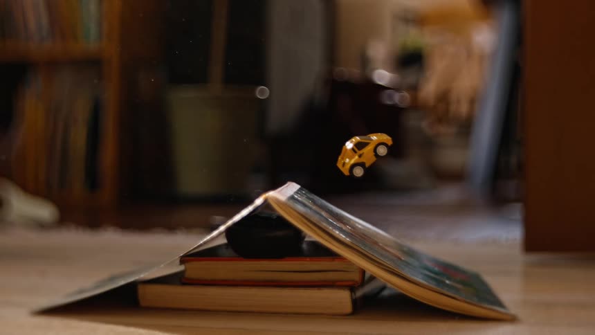 A small yellow toy car jumps off a makeshift ramp made of books in cinematic slow motion
