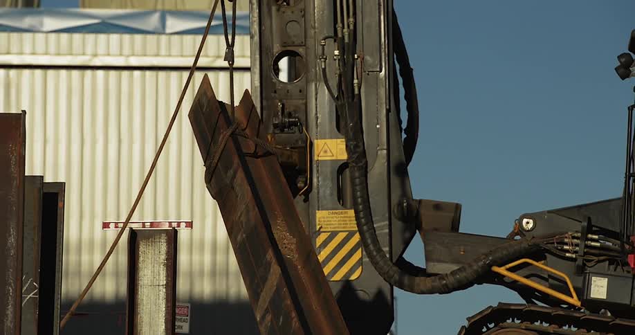 A crane lifts a rusty metal beam into the air