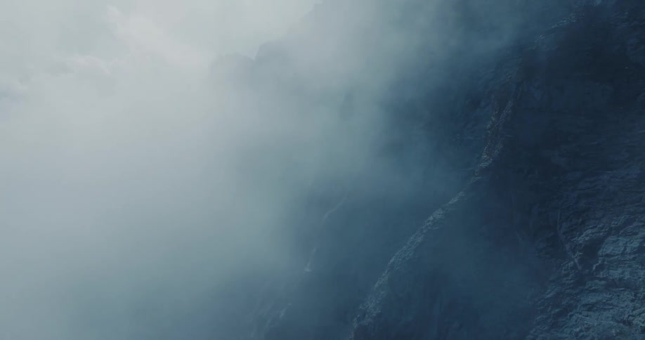 A moody and dramatic shot of thick fog rolling over a dark rock cliff face