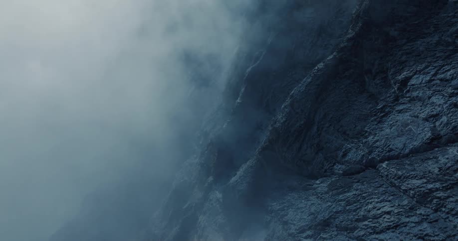 A vertical view of a mysterious rocky cliff face shrouded in moving clouds