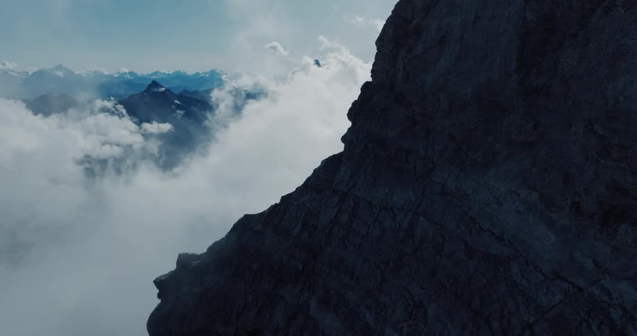 A majestic view from a dark mountain cliff face reveals a sea of clouds covering the peaks below