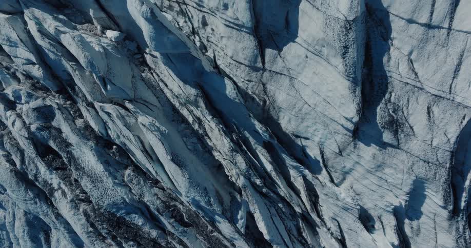 An epic top-down aerial view slowly ascends over the cracked and textured surface of a massive glacier