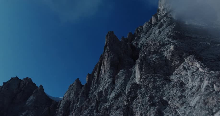 A slow and majestic push-in shot reveals the imposing, jagged peaks of a rocky mountain against a deep blue sky