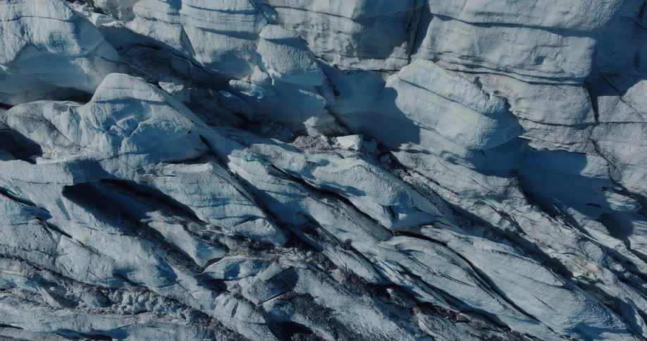 Abstract top-down aerial view of a glacier's textured surface, showing deep crevasses and icy ridges